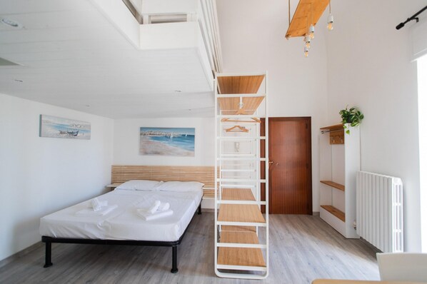 Ein modernes Schlafzimmer mit einem Bett, einem Holzkopfstück, einem weißen Kleiderschrank und einer Pflanze.