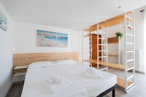 Ein modernes Hotelzimmer mit einem großen Bett, einem Holz-Kopfteil, einem Gemälde einer Küstenlandschaft und einem eingebauten Kleiderschrank mit einer Pflanze.