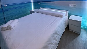 A modern bedroom with a bed, bedside tables, and a view of the ocean. - Habitación con Jacuzzi y Baño Privado (Madrid)