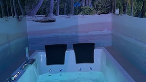 A bathtub with two black seats, surrounded by a tropical view of palm trees and a beach. - Habitación con Jacuzzi y Baño Privado (Madrid)