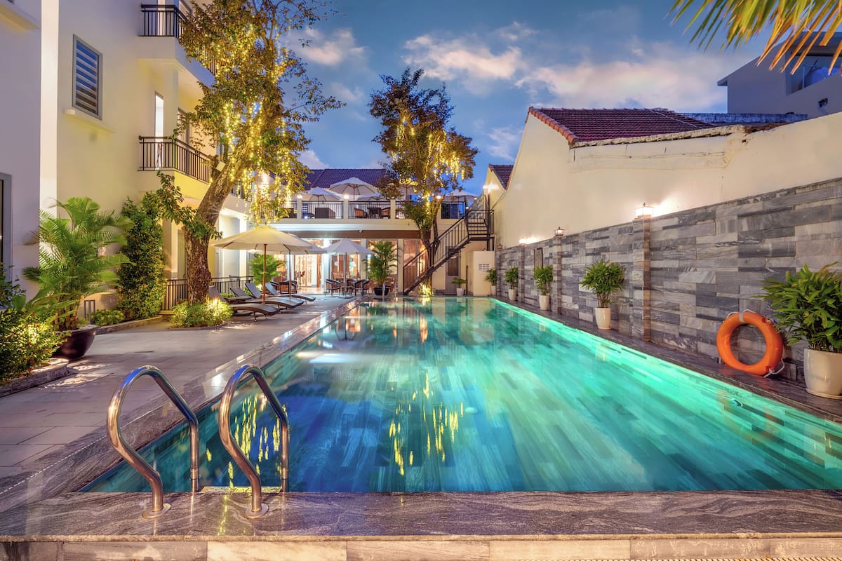 A swimming pool with a clear blue water, surrounded by potted plants and a stone wall.