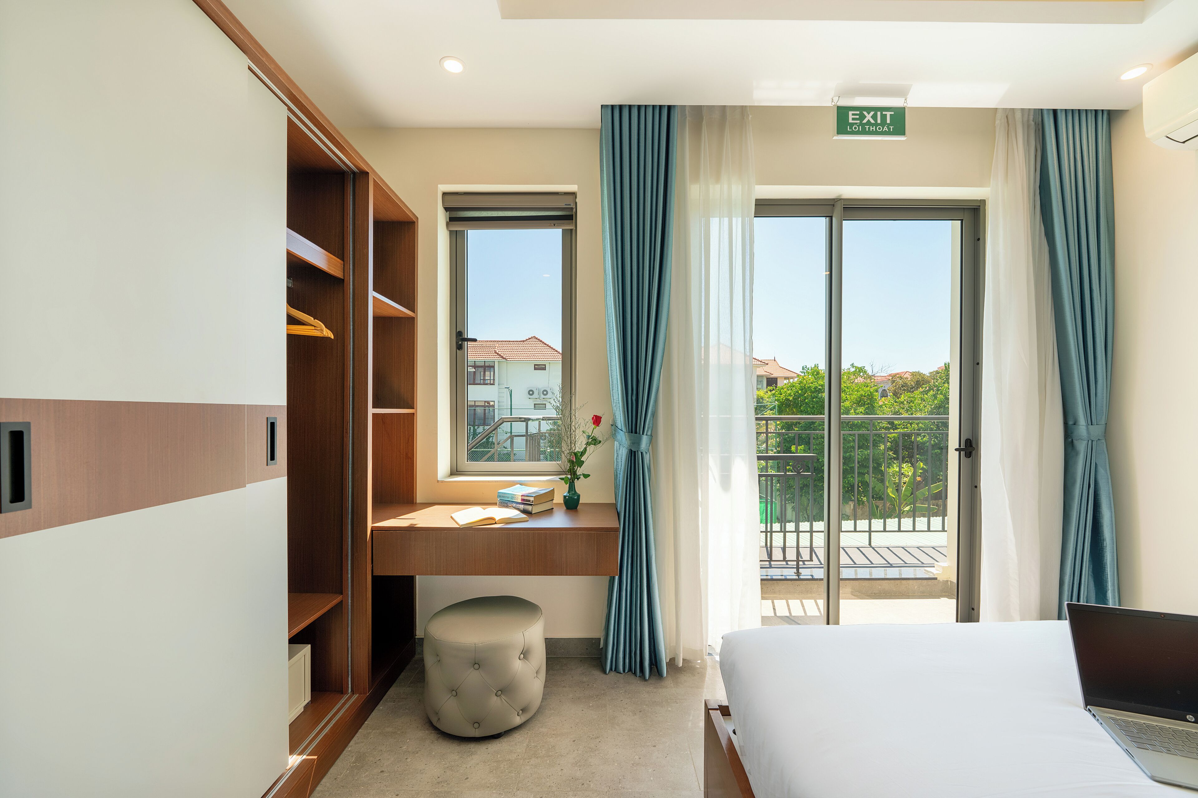 Une chambre d’hôtel avec un lit, un bureau avec un ordinateur portable, une armoire et une vue sur le balcon extérieur.