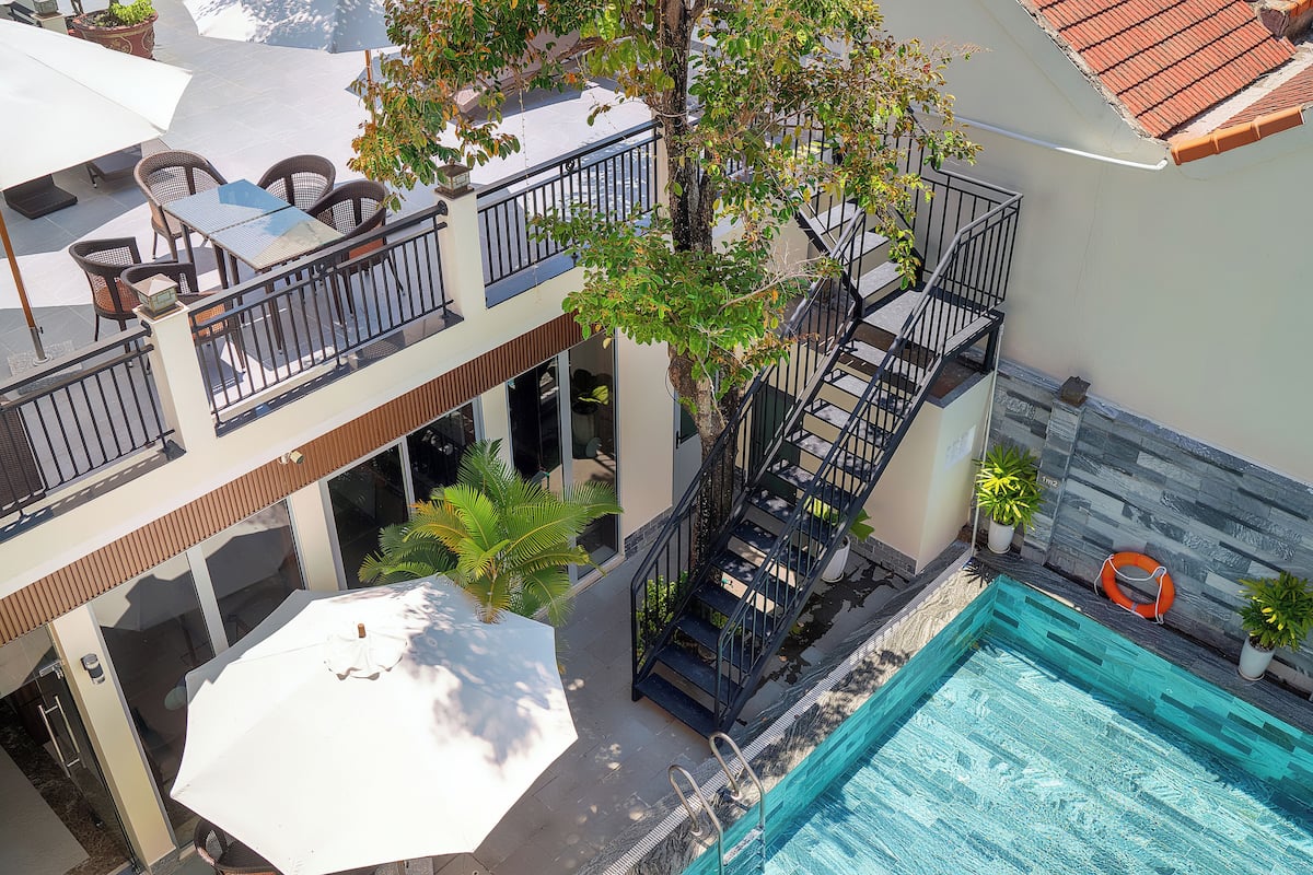 A rooftop pool area with a glass balustrade, outdoor seating, and a staircase leading to a balcony.