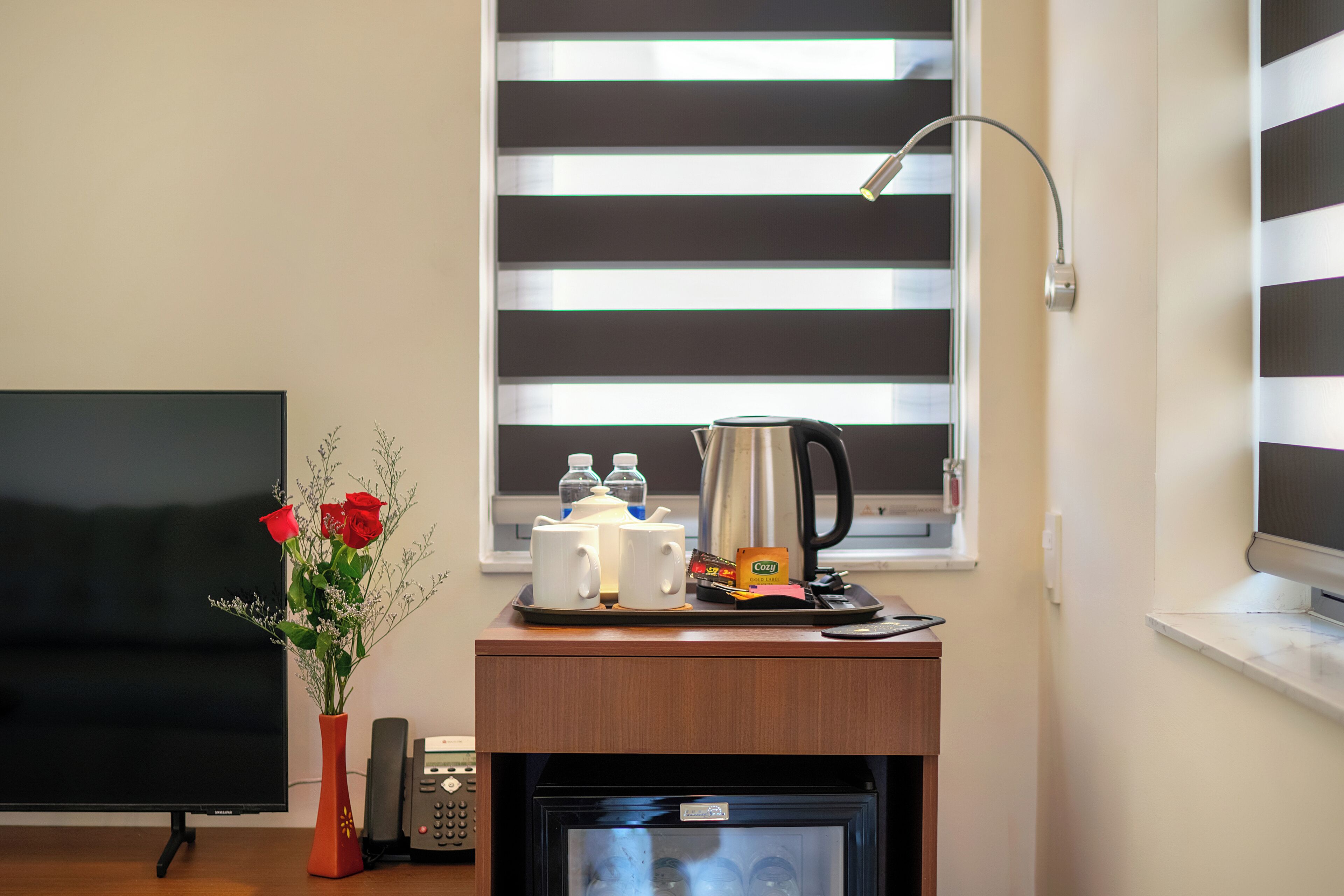 A hotel room with a flat-screen TV, a coffee station with a kettle, cups, and a small refrigerator.