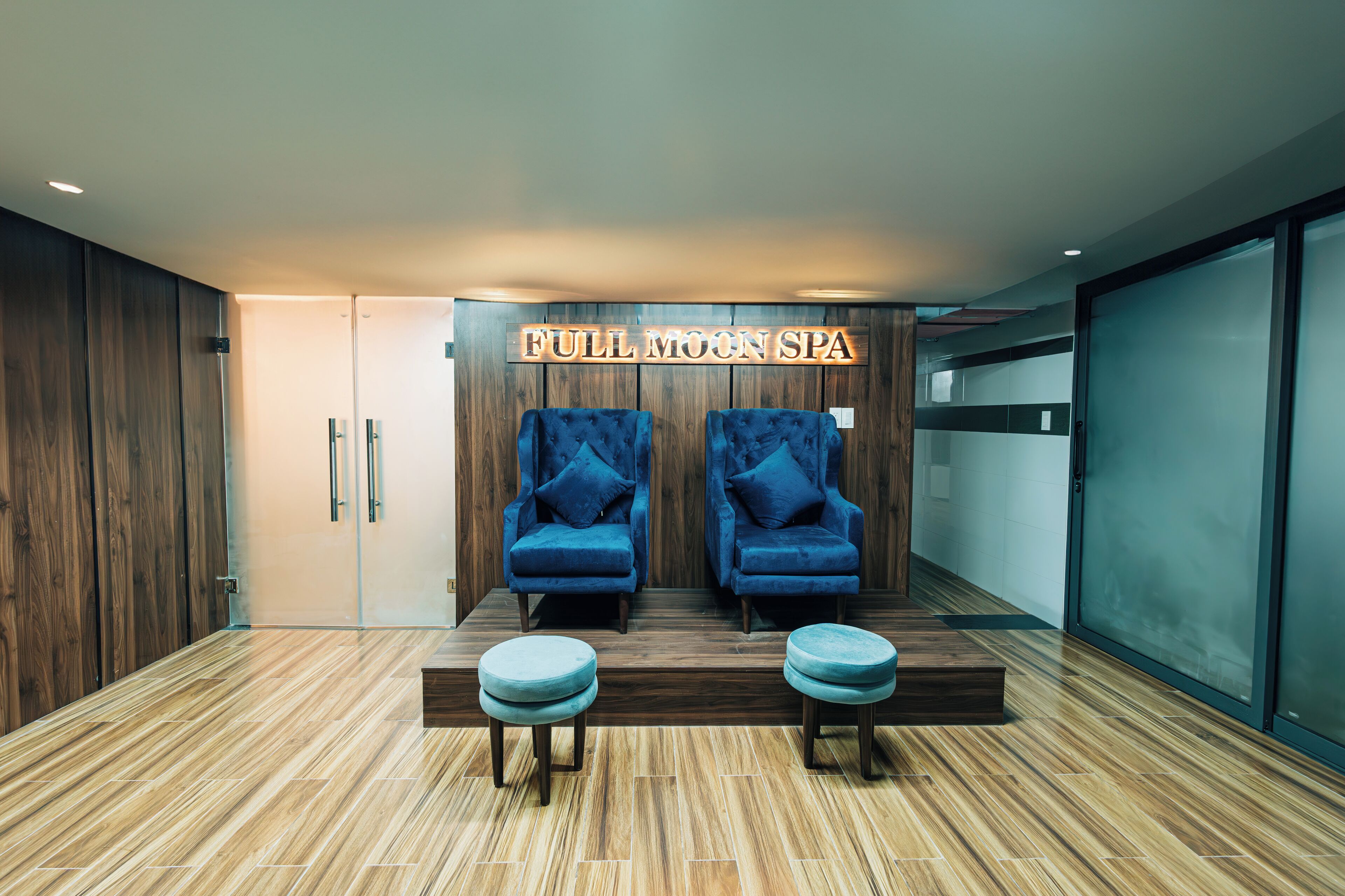 A spa area with two blue chairs and a wooden bench, a sign reading "FULL MOON SPA", and a wooden floor.