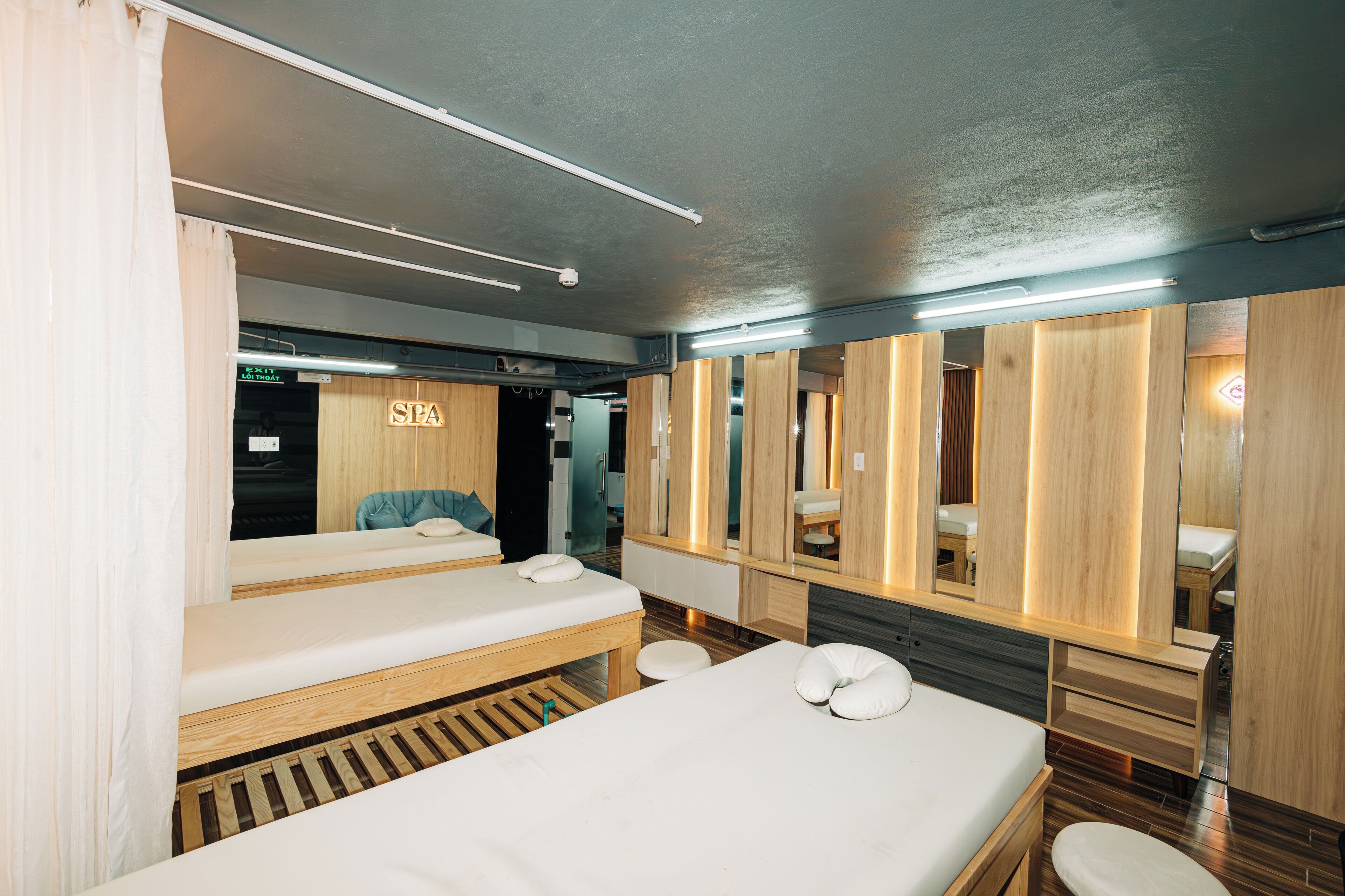 A modern spa room with wooden paneling, a large mirror, and two beds with white linens.