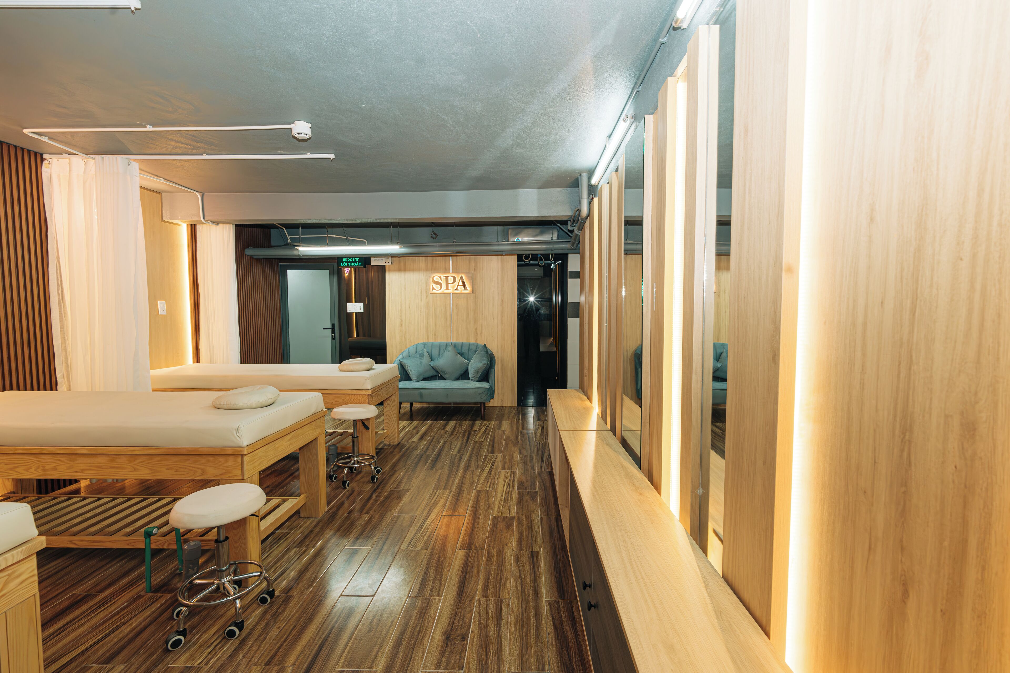 A spa room with wooden flooring, a massage table, a massage chair, and a wall-mounted sign that reads "SPA".