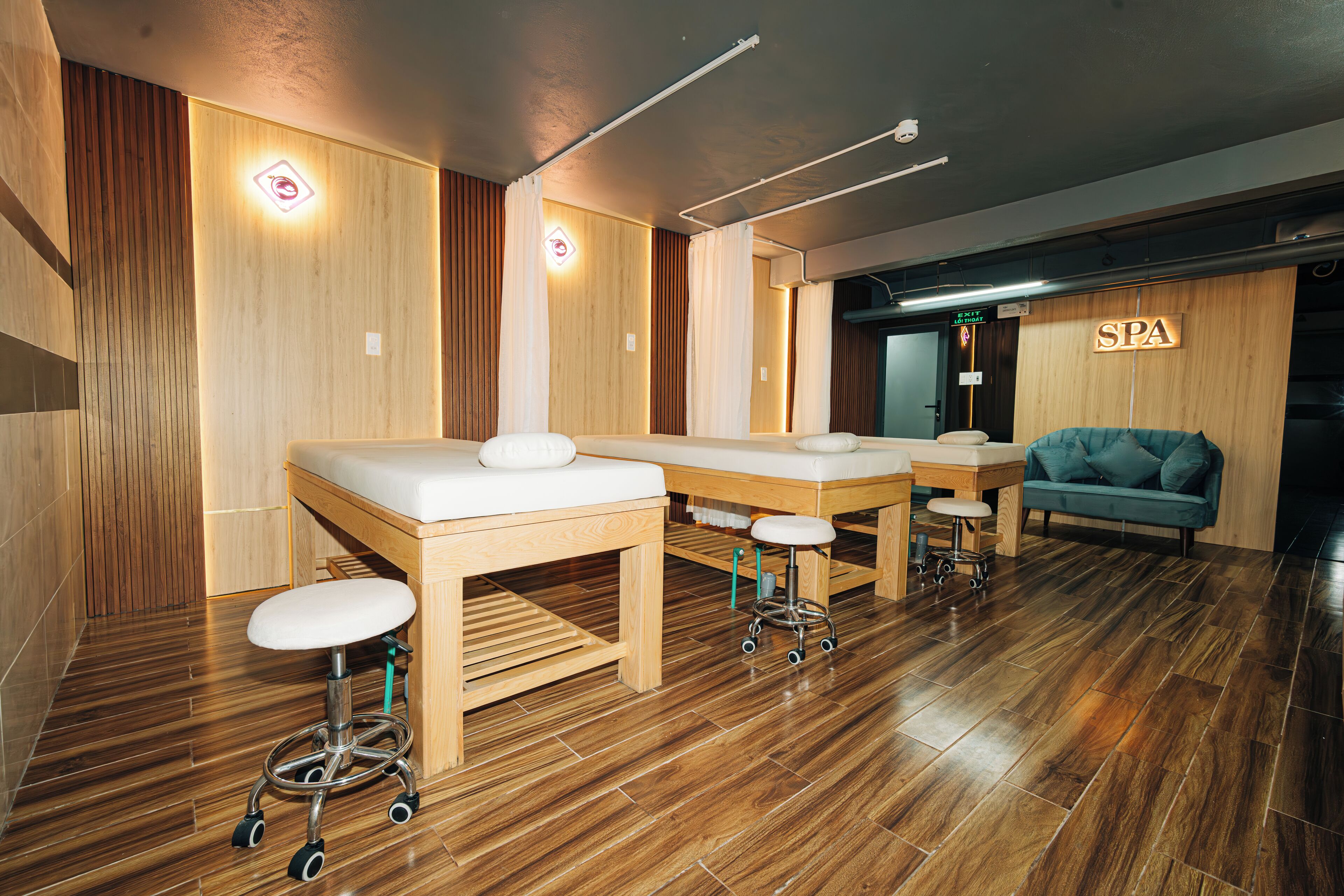 Un cuarto de spa con piso de madera, dos camillas de masaje, un sofá azul y un letrero que dice 'SPA'.