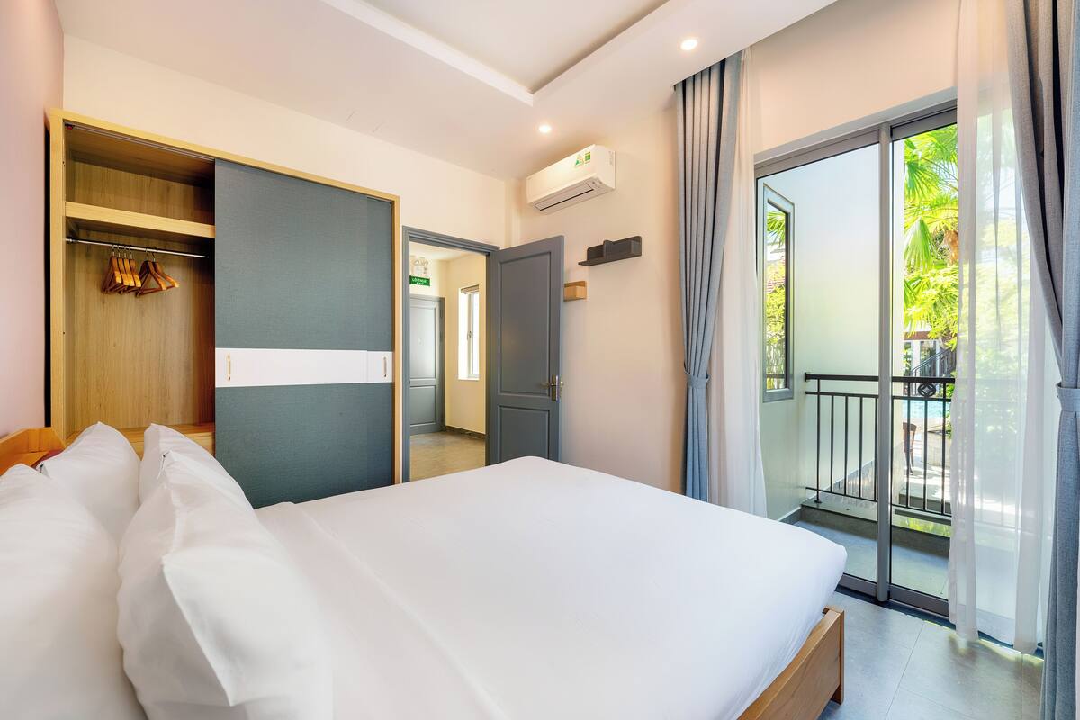 A hotel room with a bed, a wardrobe, a balcony with a railing, and an air conditioning unit.