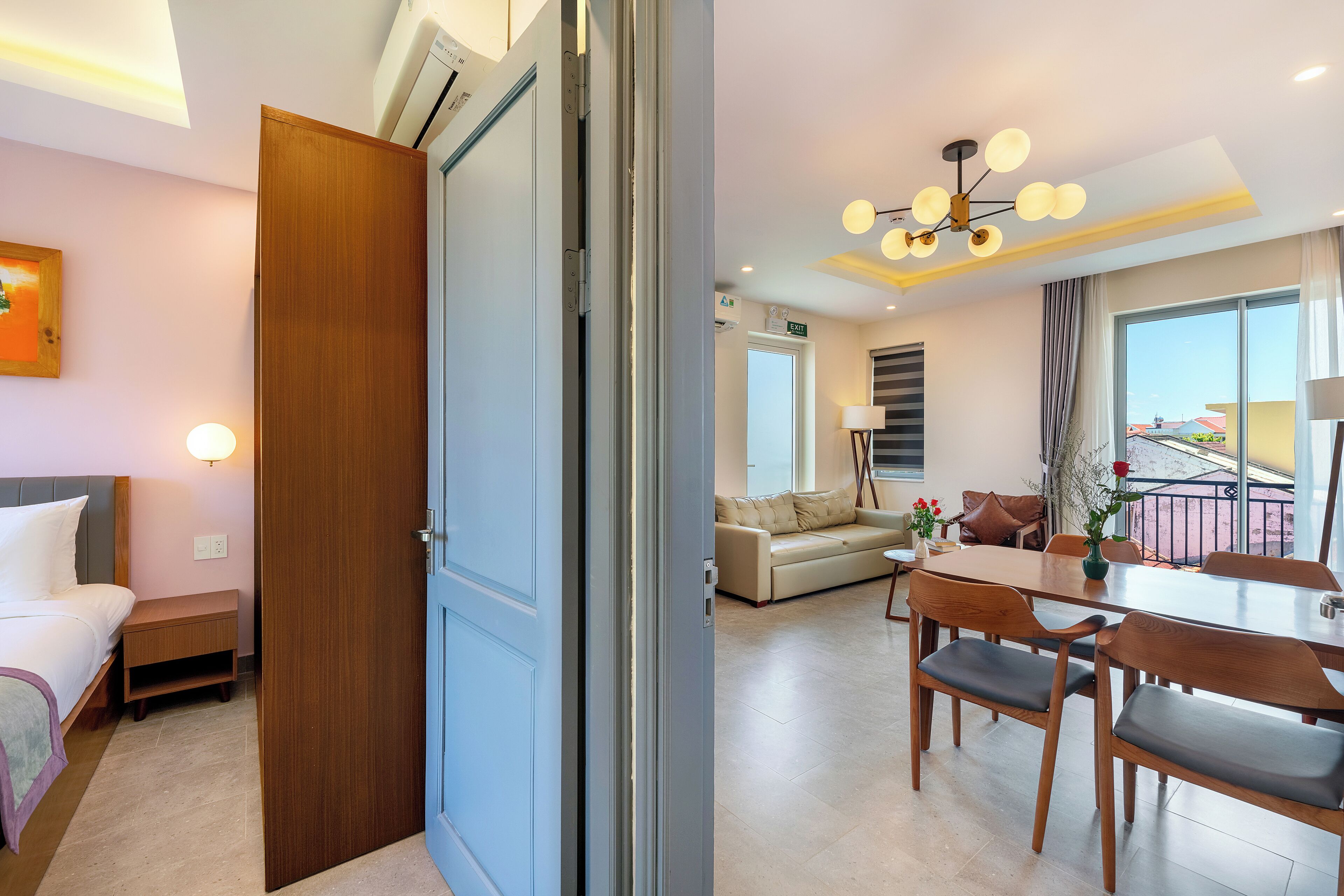 Habitación de hotel con cama, mesita de noche y puerta de madera. La habitación tiene un ventanal y vista al exterior.