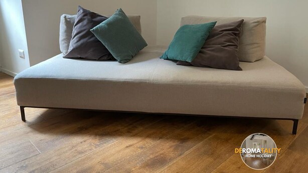 A modern sofa with two pillows, a wooden floor, and a plain wall. - Deromatality, Vatican, Colosseum, St Peter Plaza (Roma)