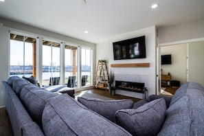 A modern living room with a large gray sectional sofa, a fireplace, and a TV mounted on the wall. - High End Home on Water & Pool! 7 night minimum. Sunday to Sunday (Saint Joseph)