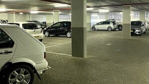 A parking garage with multiple cars parked, concrete pillars, and a tiled floor.