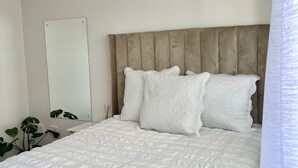 A neatly made bed with a headboard, a bedside table, and a mirror on the wall.