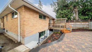 Une maison moderne avec une façade en briques, une terrasse en bois et un jardin clôturé.
