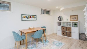 Un coin repas avec une table en bois et deux chaises bleues, un meuble blanc avec des rangements et une œuvre d’art encadrée au mur.
