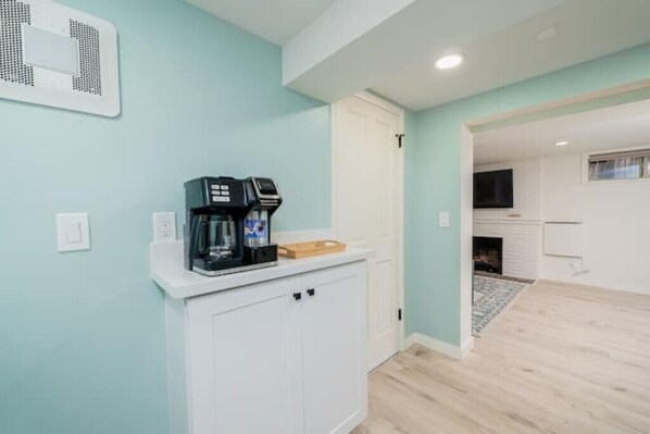 A kitchen with a coffee maker on the counter, a white cabinet, and a door leading to another room.