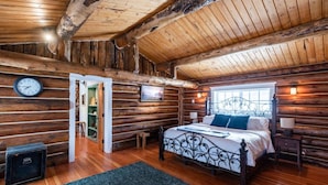 A log cabin bedroom with a bed, bedside tables, a clock, and a window.