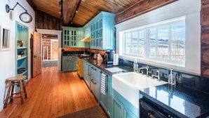 A kitchen with wooden beams, teal cabinets, and a large window.