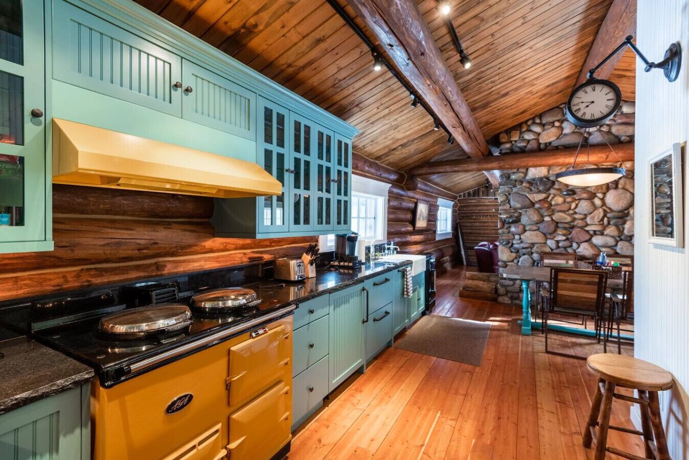 A rustic kitchen with wooden cabinets, a stone wall, and a wooden ceiling.