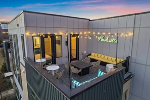 Ein moderner Außenbereich mit Sitzgelegenheiten, einem Neonzeichen, Gartenmöbeln und Lichterketten.
