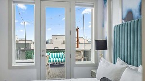 Quarto com cama, janela e vista para área externa com cadeira e mesa.