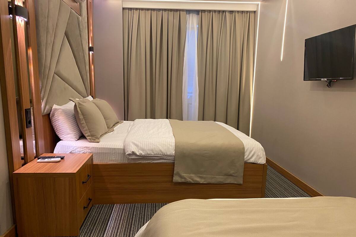 A hotel room with a bed, a bedside table, a TV, and a window with curtains.