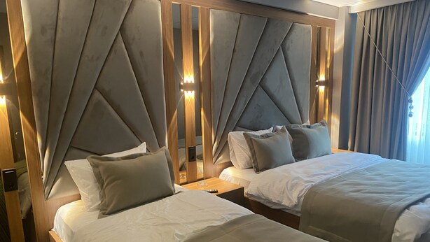 A hotel room with two beds, a wooden headboard with a geometric design, and a nightstand with a lamp. - Beşiktaş Vip İnn Hotel & Suites (Istanbul)