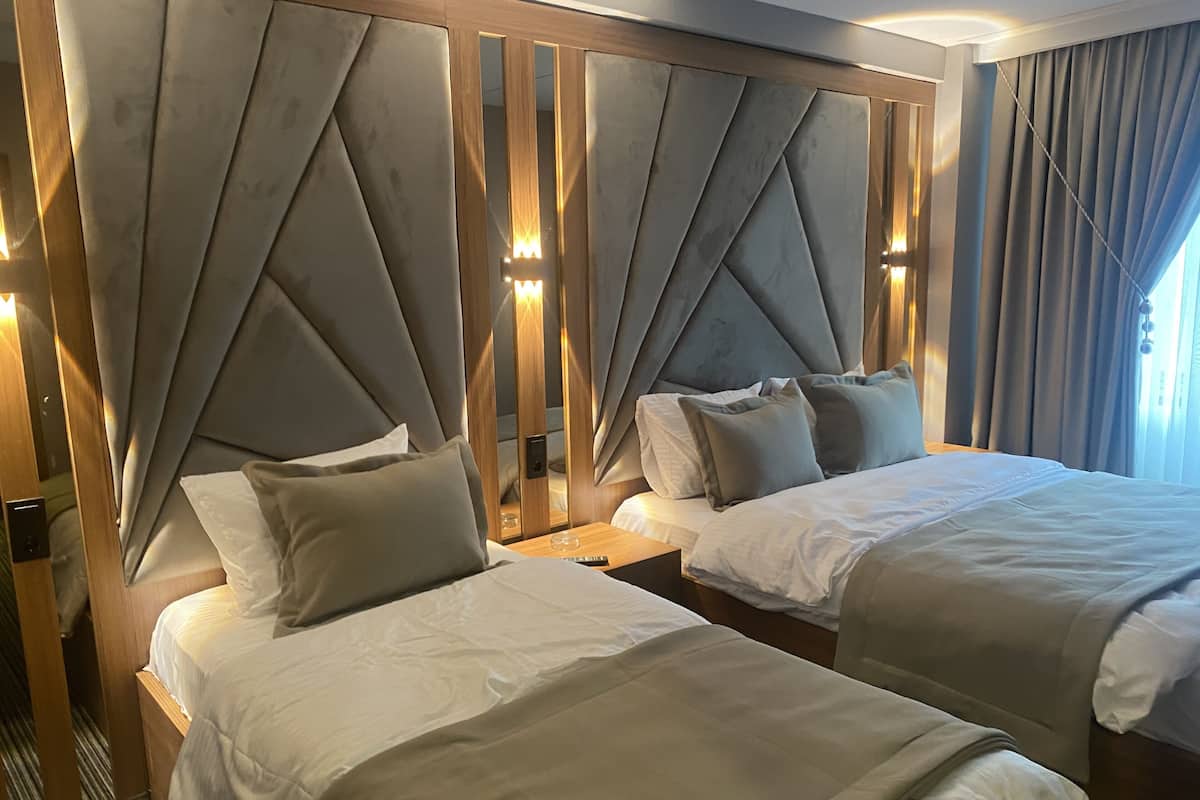 A hotel room with two beds, a wooden headboard with a geometric design, and a nightstand with a lamp.
