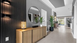 Un interior moderno con una consola de madera, un espejo redondo y plantas en macetas.