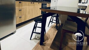 Una cocina moderna con armarios de madera, un refrigerador de acero inoxidable y una zona de comedor con taburetes.