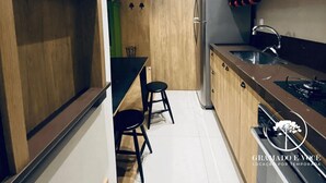Una cocina compacta con armarios de madera, un refrigerador de acero inoxidable y una encimera negra.
