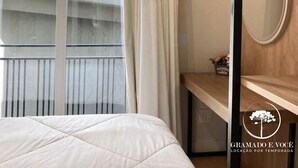 Habitación de hotel con cama, ventana con cortinas, un escritorio de madera, espejo y un adorno en la pared.
