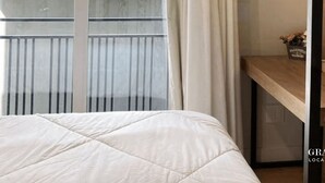 A hotel room with a bed, a window with curtains, a wooden desk, a mirror, and a decorative wall piece. - Apartamento Novo Loft One Centro Gramado (Gramado)