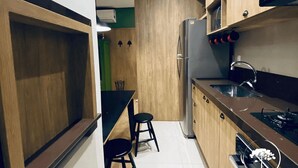 A compact kitchen with wooden cabinets, a stainless steel refrigerator, and a black countertop. - Apartamento Novo Loft One Centro Gramado (Gramado)