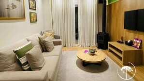 A modern living room with a sofa, a coffee table, and a television. - Apartamento Novo Loft One Centro Gramado (Gramado)