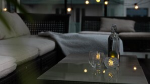 Ein modernes Wohnzimmer mit einem Glastisch, einer Couch und Blick auf ein Gebäude durch große Fenster.
