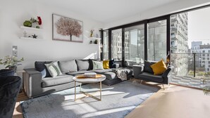 Ein modernes Wohnzimmer mit einem grauen Sofa, einem Couchtisch und einem großen Fenster mit Blick auf die Stadt.