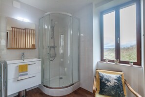 Une salle de bain dotée d’une douche à parois de verre, d’un lavabo blanc et d’une serviette jaune, ainsi que d’une fenêtre donnant sur l’extérieur.