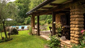 A stone building with a covered patio, a pool, and a garden area with chairs and tables.