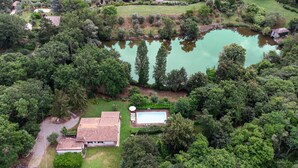 An aerial view of a property with a swimming pool, a house with a tiled roof, and dense surrounding vegetation.