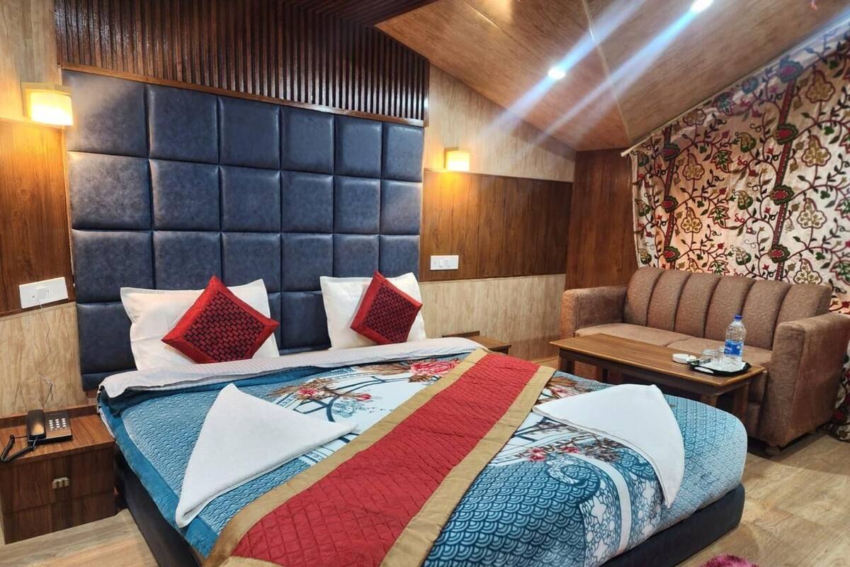 Una habitación de hotel con una cama grande, cabecera de madera, un sofá y pared con estampado.