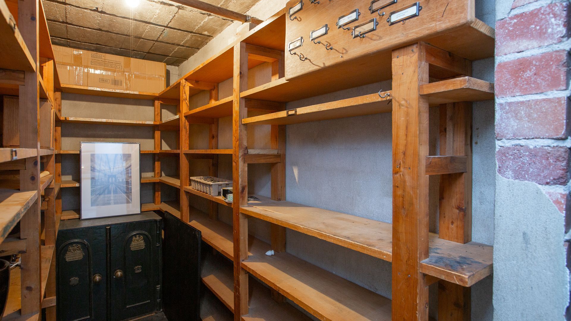 Een kamer met houten wandplanken, een ingelijst kunstwerk en een antieke kluis.