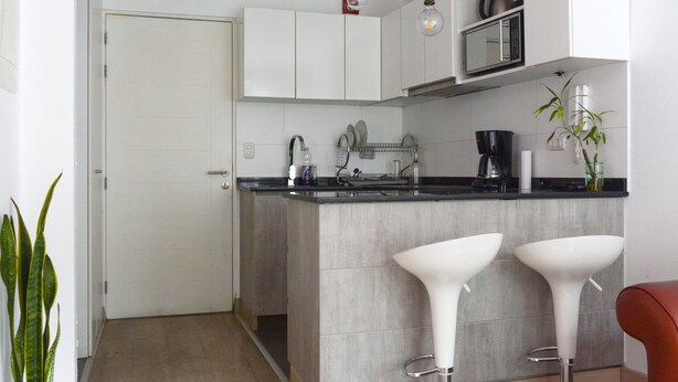 Una cocina moderna con armarios blancos, encimera negra y dos taburetes blancos.