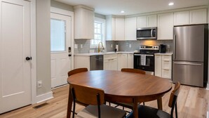 Une cuisine moderne avec des meubles blancs, des appareils en acier inoxydable et une table de salle à manger ronde en bois.