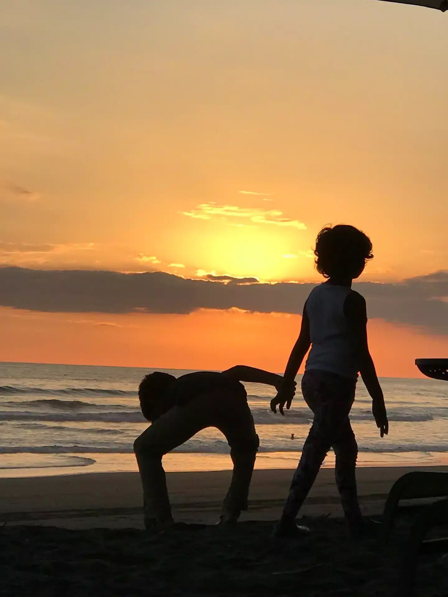 A silhouette of a person and a child walking on a beach at sunset.