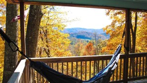 Un hamac sur une terrasse en bois donnant sur une zone boisée aux couleurs automnales.