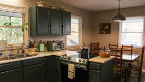 Une cuisine avec des meubles de rangement de couleur sombre, une cuisinière, un évier, un grille-pain et un coin repas comprenant une table et des chaises.