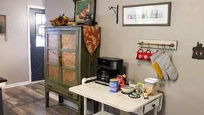 Une cuisine avec un meuble en bois, une machine à café, une table sur laquelle sont posés des ustensiles de cuisine, et un porte-ustensiles fixé au mur, contenant des maniques de four.