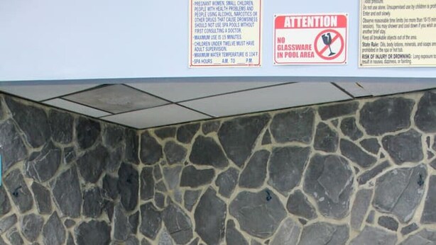 Muro de piedra que rodea una bañera de hidromasaje con un grifo metálico y dos esteras negras.